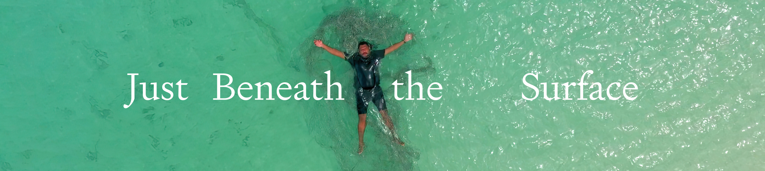 Just Beneath the Surface. Jimmy Thaiday a Torres Strait Islander man lies on his back in the clear ocean, he has a ghost net entangled in his body. 